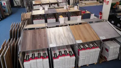 Übersicht einer Verkaufsfläche bei TTL Heilbronn mit großformatigen Vinylbodenmustern in Holzoptik. Verschiedene Farb- und Oberflächenvarianten sind auf Ausstellungstischen präsentiert; darunter stehen geordnete Musterkollektionen und Produktunterlagen.