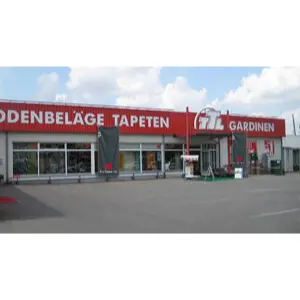 Außenansicht eines Fachgeschäfts in Heilbronn mit Beschilderung für Bodenbeläge, Tapeten und Gardinen. Die Verkaufsräume liegen an einem weitläufigen Parkplatz unter bewölktem Himmel.